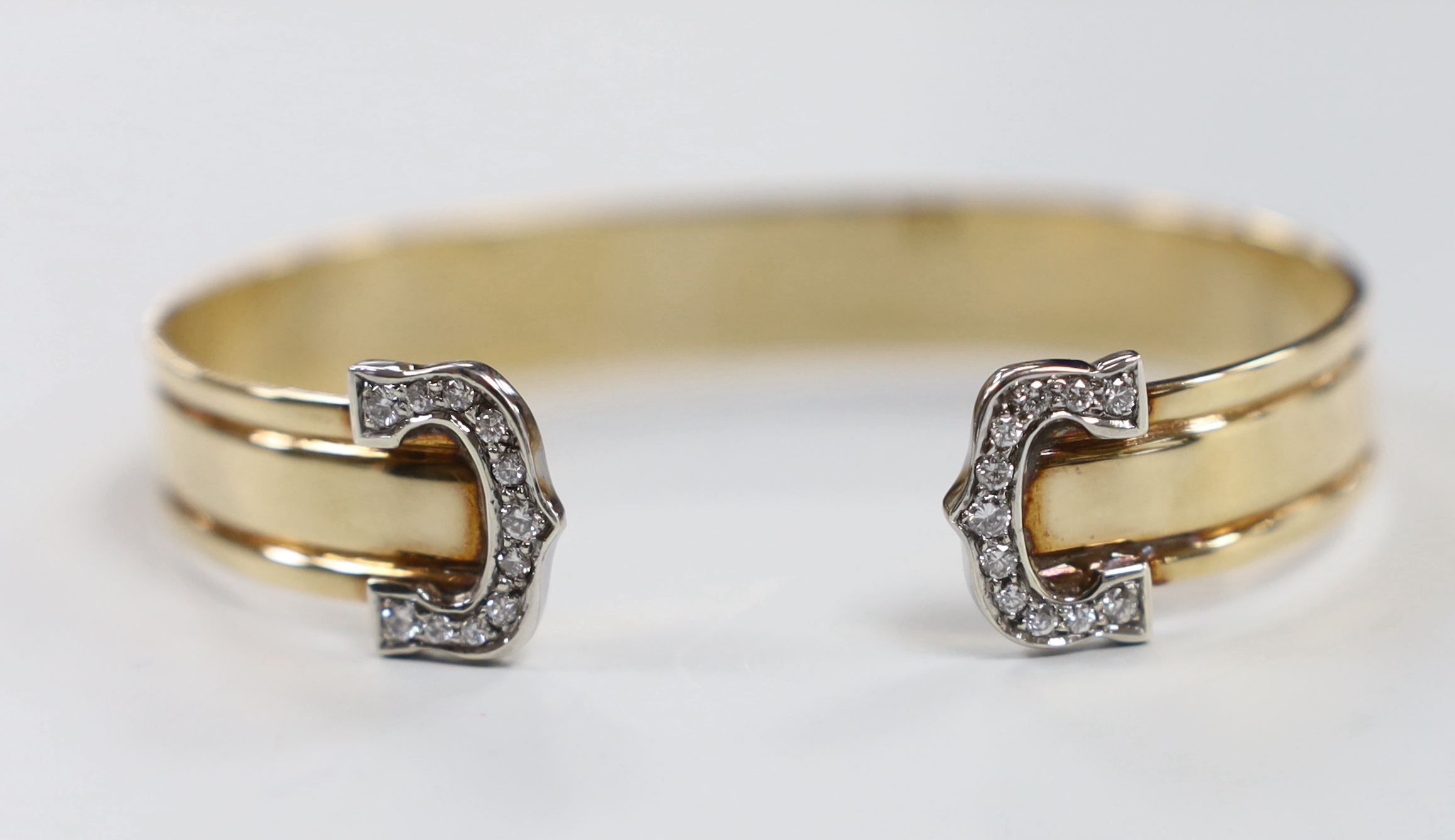 A yellow metal and diamond chip cluster set open work bangle, interior diameter approx. 66mm, gross weight 23.3 grams.